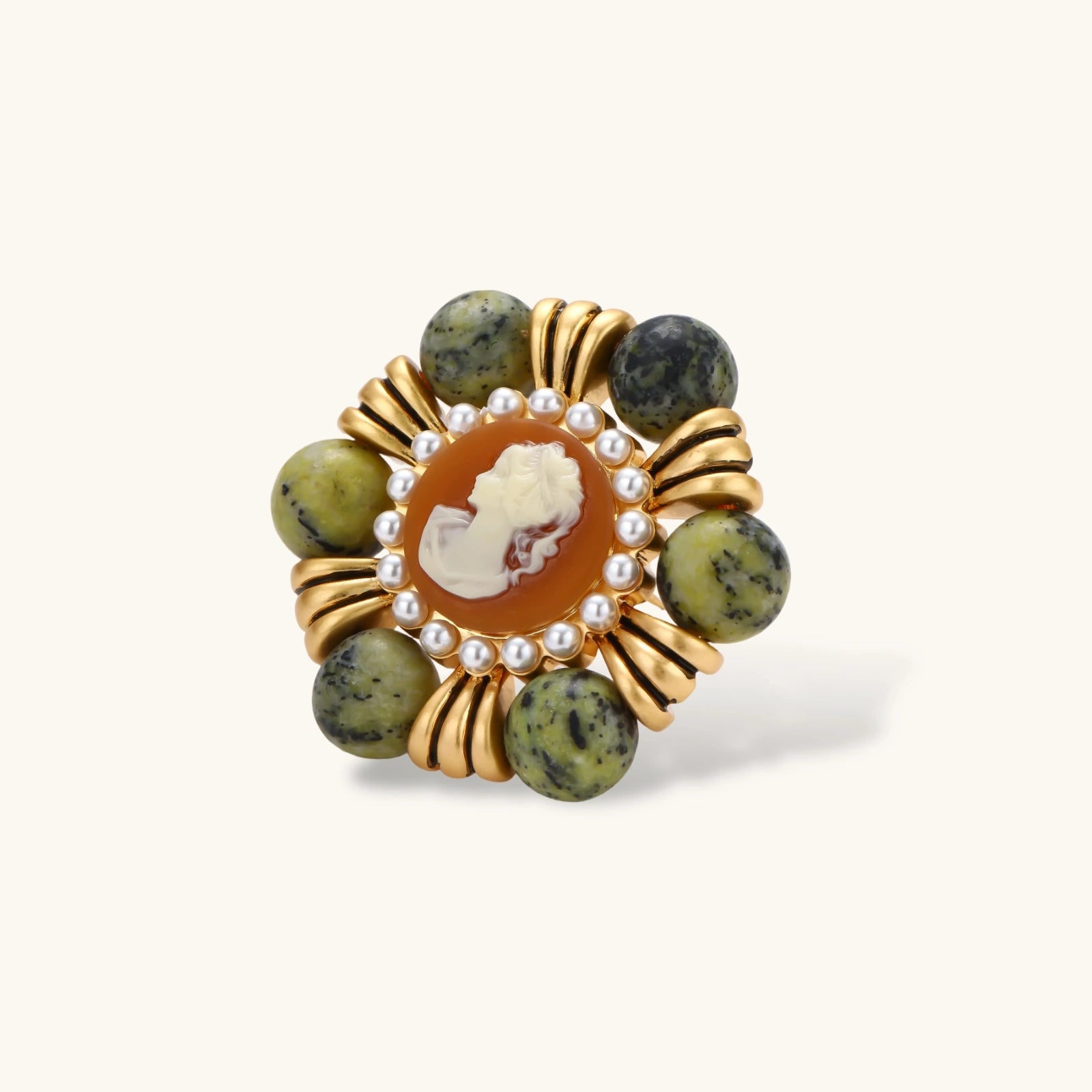 Ornate gold-plated brooch with central cameo, radiating spokes, pearl border, and green marbled natural stones on white background.