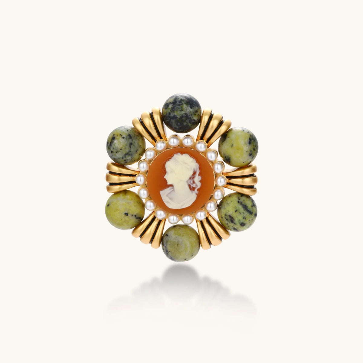 Ornate gold-plated brooch with central cameo, radiating spokes, pearl border, and green marbled natural stones on white background.