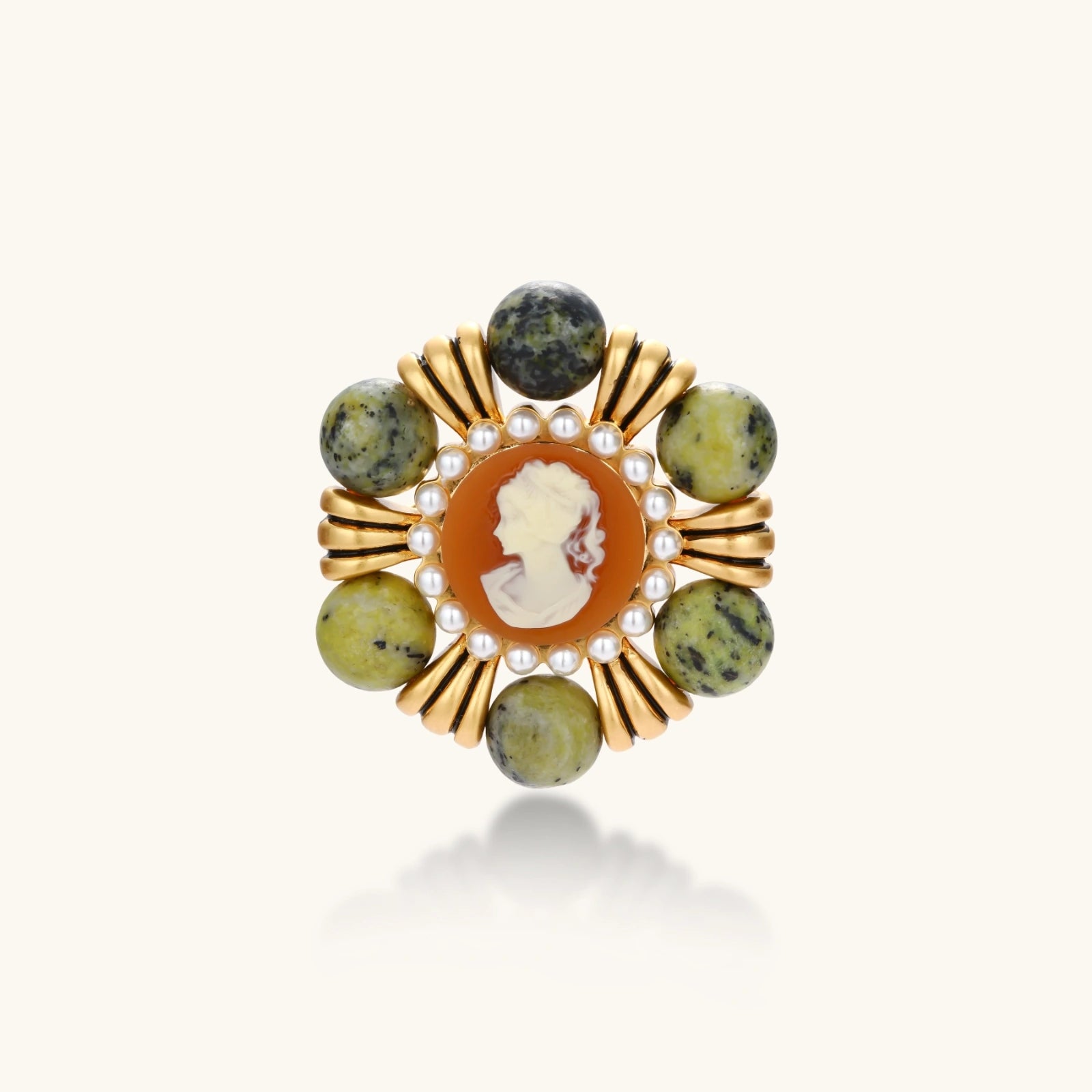Ornate gold-plated brooch with central cameo, radiating spokes, pearl border, and green marbled natural stones on white background.