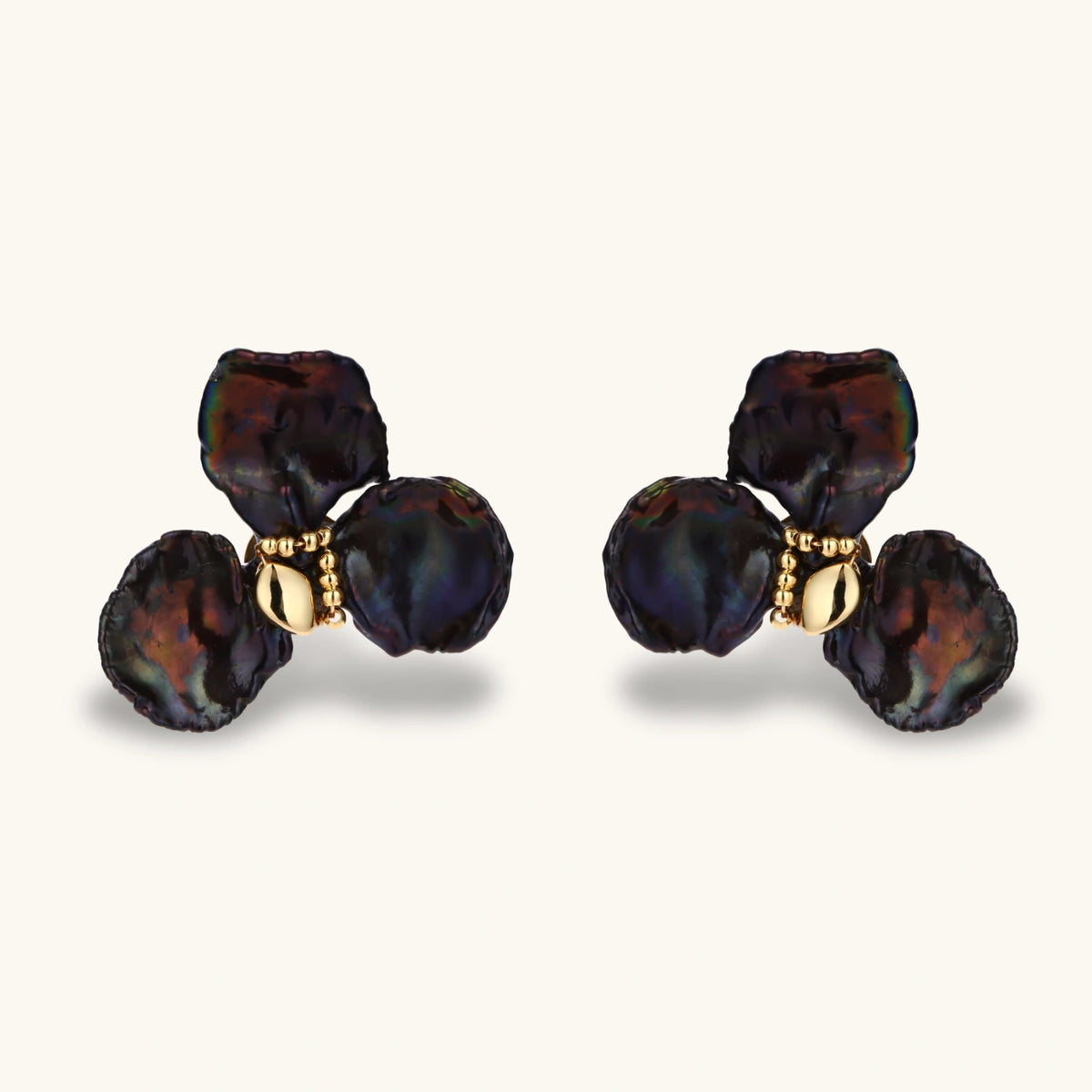 Dark iridescent baroque pearls arranged in flower pattern with 18K gold-plated center on cream background.